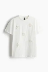 Remera blanca de algodón con cuello redondo y apliques de flores en el frente.