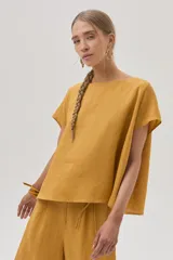 Blusa color mostaza confeccionada en lino, con cuello bote y mangas cortas.