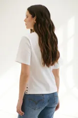 Remera blanca de algodón de corte recto, con cuello redondo y mangas cortas. Presenta detalle de aberturas laterales con ojales metálicos.