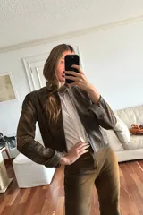 Conjunto de campera corta y falda marrón con efecto vintage. La campera es de cuero ovino con cierre frontal y cuello alto. La falda es corta y acampanada.