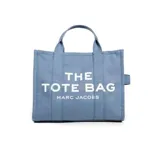 Bolso tote negro de lona con asas de mano y correa bandolera ajustable. Estampado frontal con la leyenda "THE TOTE BAG MARC JACOBS" en letras blancas.