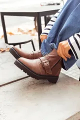 Bota corta color marrón de cuero, con hebilla metálica y cierre lateral.