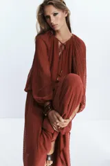 Blusa color ladrillo con textura de lunares, cuello redondo con cordón ajustable con borlas, manga larga abullonada con puños elásticos y ruedo elástico.