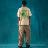 Remera oversize color beige con estampado en la espalda de una taza de café con cara sonriente, un cenicero con un cigarrillo y la frase "420 Breakfast Club. Wake and bake everyday".