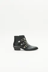 Bota de caña corta de cuero negro con tres tiras cruzadas decoradas con remaches, hebillas y puntera metálica. Tiene cierre lateral y taco ancho de 4 cm con vira metálica.