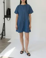 Vestido corto de denim azul, con cuello redondo y mangas cortas amplias. Presenta un corte ligeramente entallado y un cinturón de cadena metálica con eslabones circulares.