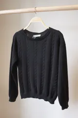 Sweater negro de punto con cuello redondo y diseño de ochos verticales en el frente.