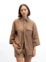 Camisa marrón claro de lino con mangas 3/4, cuello clásico, cierre frontal con botones, bolsillo de parche en el pecho y corte holgado. Marca Gaya.