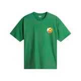 Remera de manga corta color verde, corte holgado (loose fit), con un pequeño parche circular estampado en el pecho con motivos naranjas y blancos.
