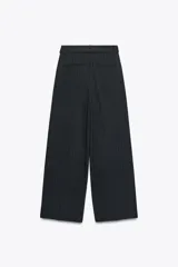 Pantalón negro con finas rayas verticales blancas, de tiro alto y corte ancho. Incluye cinturón de lazo en el mismo tejido, bolsillos laterales y pinzas.