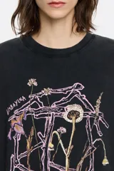 Remera negra de algodón con cuello redondo y manga corta. Estampado frontal con diseño floral abstracto en tonos rosa y marrón.