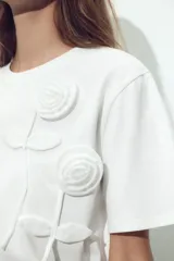 Camiseta blanca de cuello redondo y manga corta con detalle de flores con volumen en delantero a tono.