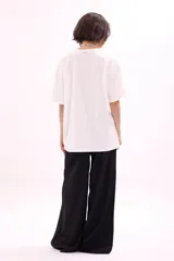 Remera blanca de algodón, corte oversize, con cuello redondo y manga corta. Presenta un estampado frontal con varias reposeras y hamacas de playa, y el texto "LA SIESTA".