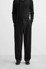 Pantalón negro de corte amplio, con pliegues frontales, bolsillos laterales y traseros de ojal. Incluye cinturón de la misma tela con hebilla metálica.