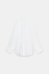 Camisa blanca amplia de cuello solapa y manga larga. Tiene un bolsillo de plastrón en el pecho, bajo asimétrico y cierre frontal con botones.