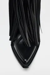 Bota de cuero negra con estilo cowboy, caña media y punta fina. Presenta detalle de flecos largos en el cuerpo y tiradores laterales.