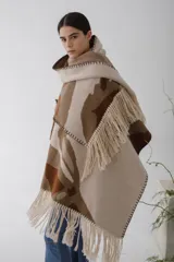 Ruana de lana con diseño abstracto en tonos beige, marrón y blanco. Presenta flecos en el borde inferior y capucha.