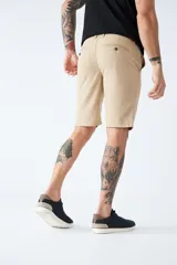 Bermuda color beige de corte chino, con bolsillos laterales, cierre con cremallera y botón, presillas para cinturón y logo bordado. Confeccionada en lino y algodón.