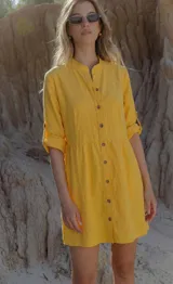Vestido camisero amarillo de lino, corte recto y calce relajado, con cuello mao, escote frontal abotonado, mangas 3/4 con tira y botón para arremangar, y largo medio.
