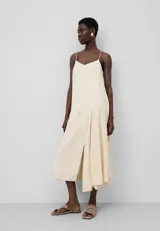 Vestido midi color crema con breteles finos, escote en V y corte asimétrico. Presenta una sección lisa y otra con bordado calado.