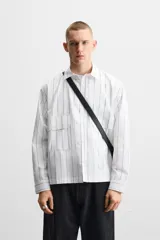 Camisa cropped fit confeccionada en tejido de algodón a rayas verticales negras sobre fondo blanco. Cuello solapa y manga larga acabada en puño con botones. Bolsillos frontales de plastrón con solapa. Cierre frontal de botonadura.