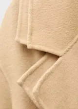 Abrigo largo color beige con cuello con solapa, cinturón ajustable y chaleco interior desmontable.