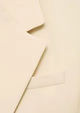 Blazer color crema con cuello de solapa, doble botonadura frontal, corte recto y mangas largas con puños abotonados. Prenda de la colección de evento.