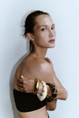 Set de tres pulseras rígidas: una dorada de metal y dos de resina, una color crema y otra marrón, ambas con tachas doradas.