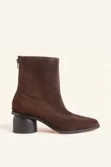 Bota corta de cuero vacuno color marrón oscuro, con diseño sin forro y taco cilíndrico de madera tallada a mano. Presenta cierre posterior y punta redondeada.