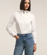 Camisa blanca de tricolina con cuello padre, abotonada al frente con detalle ondulado y mangas largas.