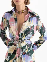 Camisa de satén con estampado multicolor, cuello camisero, mangas largas y puños con botones dorados. Cierre frontal oculto y lazos en la cintura para ajustar la silueta.