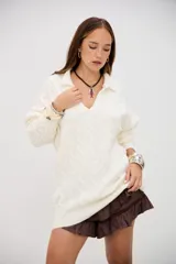 Sweater de punto grueso color crudo, con cuello polo y escote en V. Presenta un diseño de trenzas en toda la prenda y es de corte holgado.