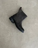 Botín de cuero vacuno color negro con detalle de textura en la caña, corte a media pierna, suela de goma y cierre lateral.