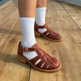 Sandalias franciscanas de cuero color marrón con tiras entretejidas, hebilla lateral y taco bajo de madera.