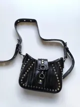 Cartera negra de charol con forma de media luna y tachas plateadas. Tiene correa de hombro ajustable y cierre con hebilla.