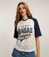 Remera de encaje blanco con mangas cortas raglán azul marino, cuello en V y estampado frontal con la inscripción "Kansas League Est. 1995".