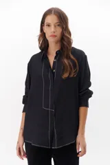 Camisa negra de manga larga con cuello clásico y cierre frontal con botones. Presenta costuras decorativas en color blanco.