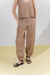 Pantalón de lino color marrón, con corte tipo barrel, tiro medio, pretina ancha con doble abotonadura, bolsillos laterales y pinzas en el frente. Ruedo con presilla permitiendo usarlo recto o fruncido al tobillo.