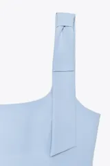 Top blanco de tejido elástico con escote cuadrado y tirantes con lazos decorativos. Tiene forro interior y cierre lateral con cremallera oculta.