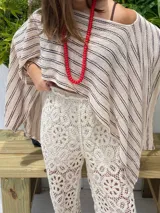 Poncho de tejido de punto, color crudo con rayas horizontales negras. Diseño holgado y asimétrico, con escote amplio.