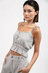 Top gris de lino con breteles finos con nudo, escote recto, corte crop con elástico en la cintura y botones frontales.