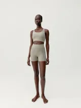 Short deportivo color arena, de tiro alto, confeccionado en tejido técnico con costuras termoselladas y cinta reflectante decorativa.