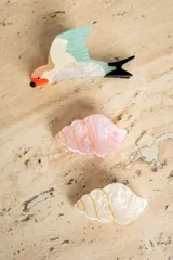 Broche con forma de colibrí con cuerpo blanco, cabeza naranja, pico negro, ala celeste y cola negra.