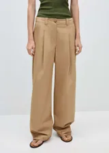Pantalón de vestir color beige, de corte wide leg, tiro medio, con pinzas delanteras, bolsillos laterales y cierre con cremallera y botón.