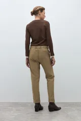 Pantalón negro de vestir, corte recto y tiro alto, con pliegues frontales y puños doblados. Se complementa con un cinturón fino negro con hebilla metálica en forma de símbolo.