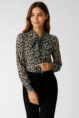 Blusa de poliéster estampada en tonos blanco y negro, con cuello a la base y lazo al cuello.