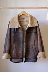 Campera gamulán marrón con cuello y puños de piel sintética color beige. Cierre frontal con cremallera y bolsillos laterales.