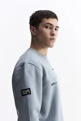 Buzo blanco de algodón con cuello redondo, puños y bolsillos laterales. Presenta un estampado en la espalda con cuatro imágenes de plantas en tonos sepia y texto.