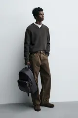 Mochila marrón oscuro de cuero, con compartimento principal con cierre de cremallera, bolsillo interno plano y bolsillo interno con cremallera. Bolsillo frontal con cremallera, parte posterior acolchada con banda de sujeción para equipaje, asa de mano y dos asas de hombro ajustables.