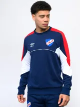 Buzo de felpa azul marino, con mangas largas, cuello redondo y puños acanalados. Presenta cortes en blanco y rojo en la parte superior, logo de Umbro bordado en el pecho y escudo del Club Nacional de Football.